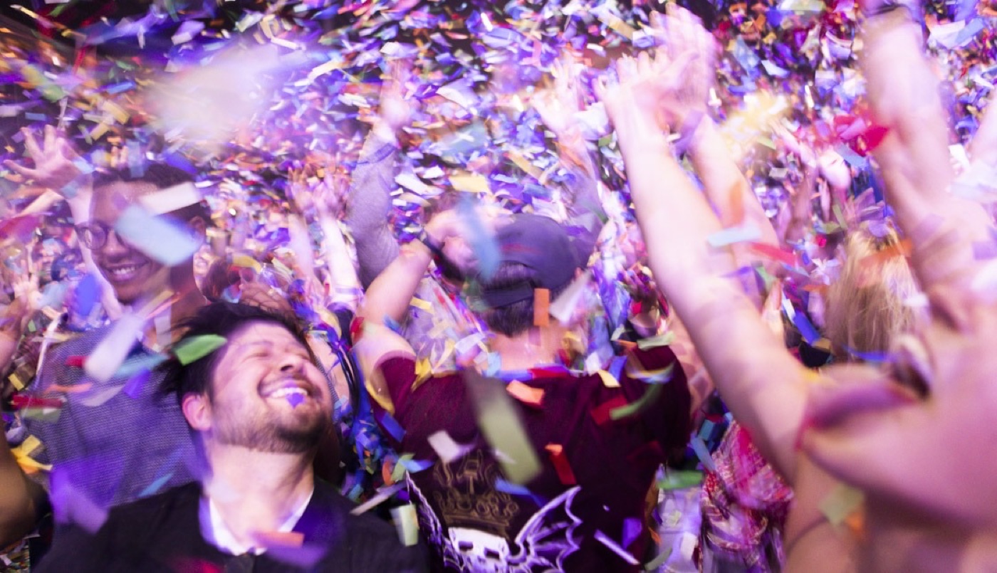 Fans laugh with their arms up as a blizzard of confetti comes down on them.