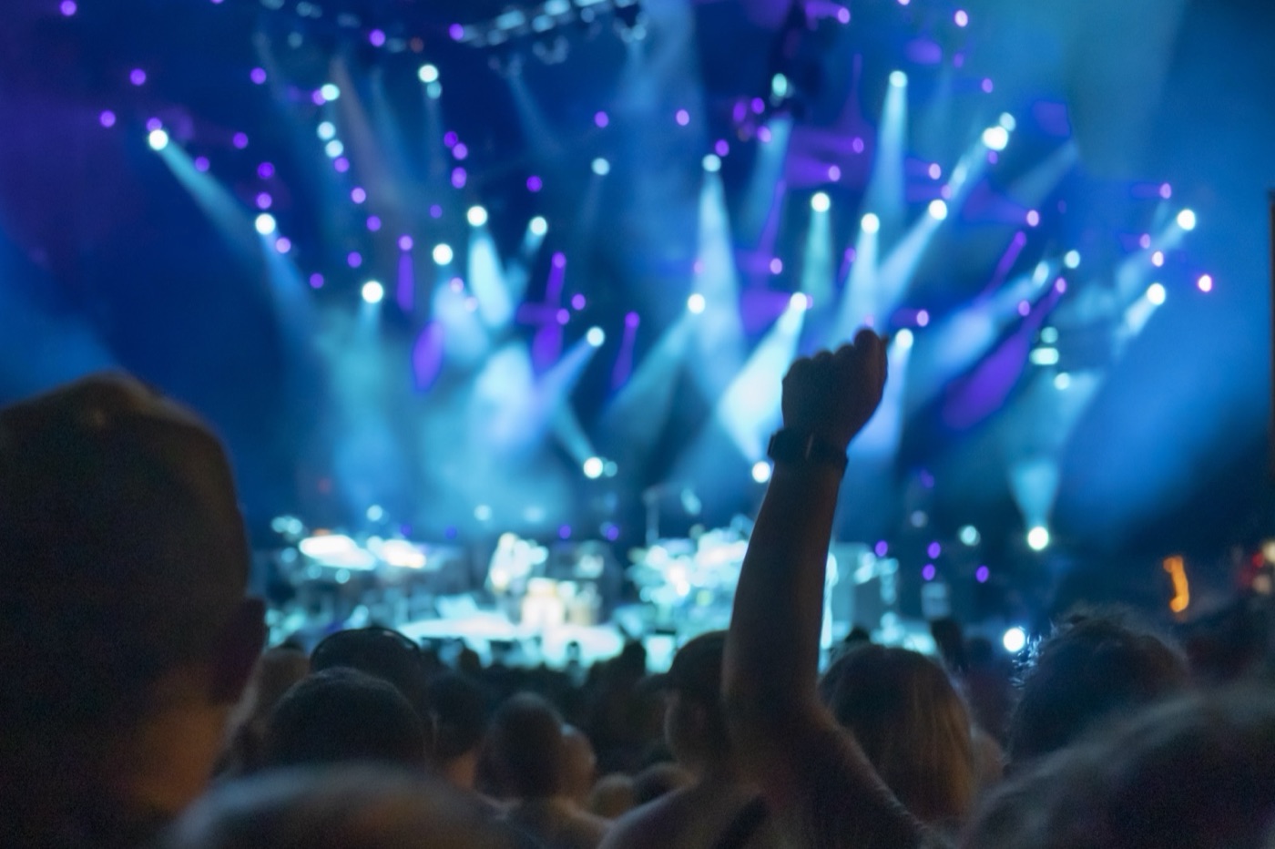 A fan raises a fist in front of a blurred stage washed in blue and violet spotlight beams.