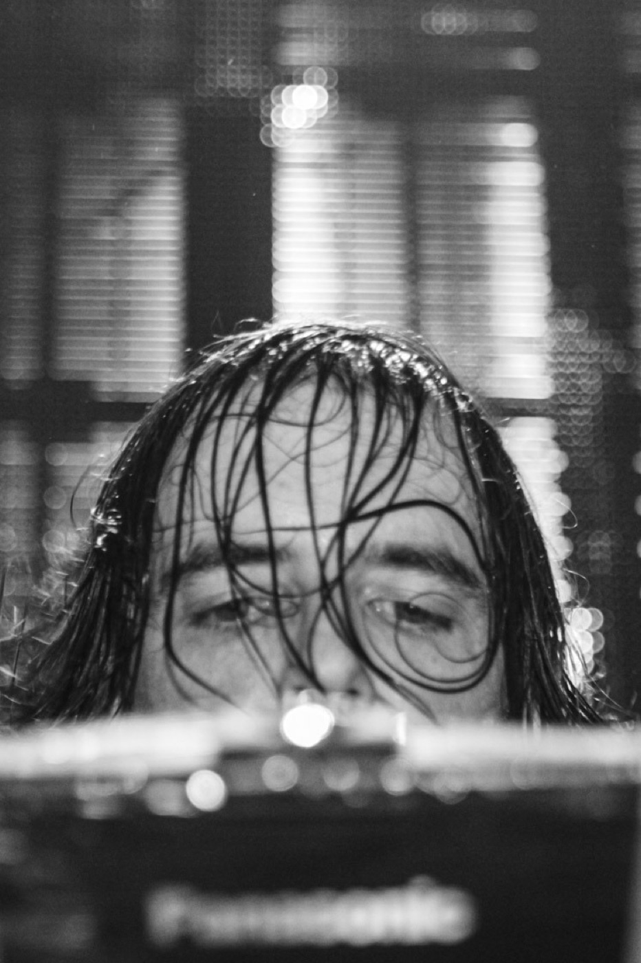 In black and white, Girl Talk peers over his gear with sweat-soaked hair plastered across his face.