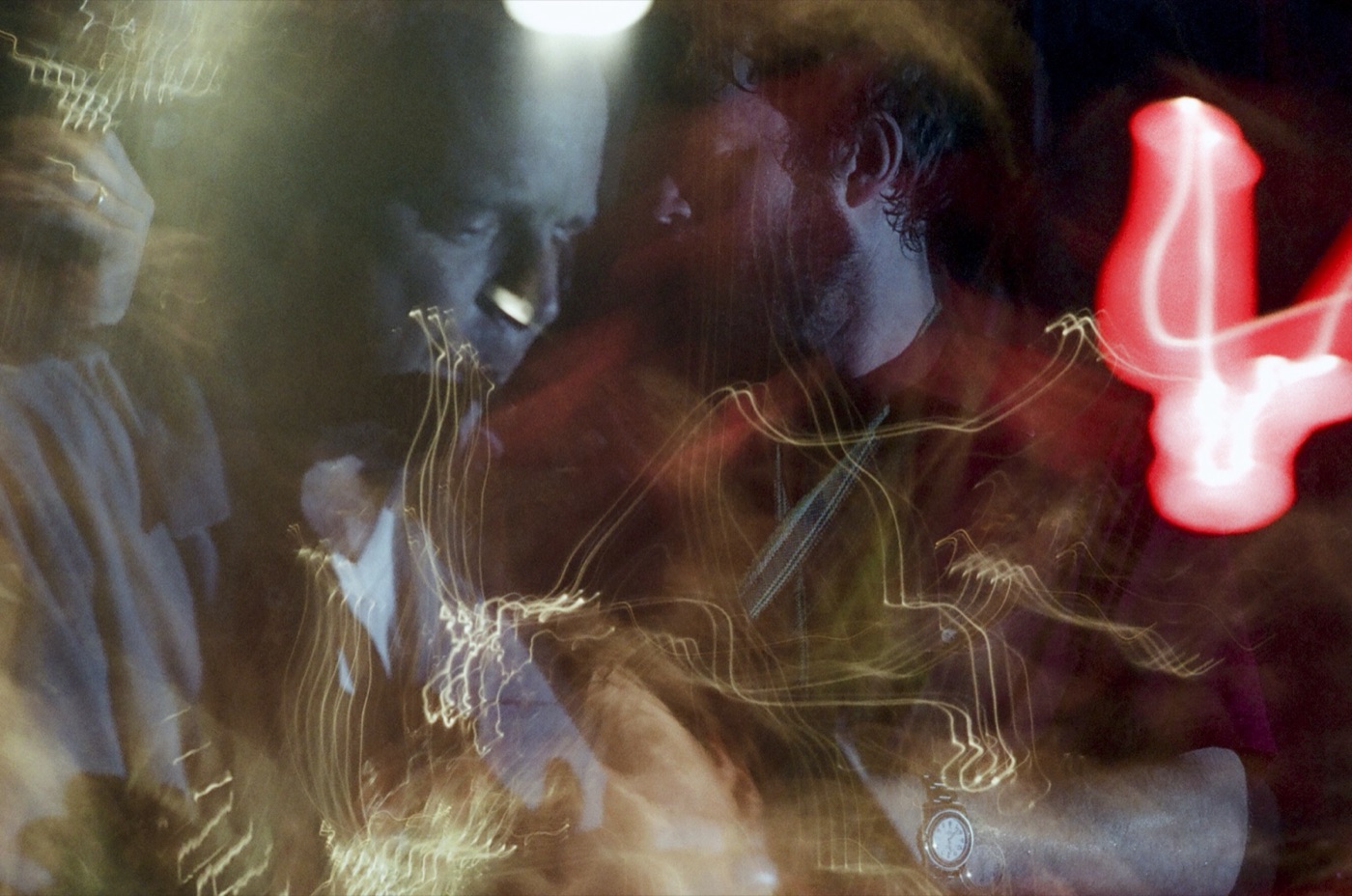 A long exposure turns faces and stage lights into swirling light trails, with a red neon squiggle on the right.