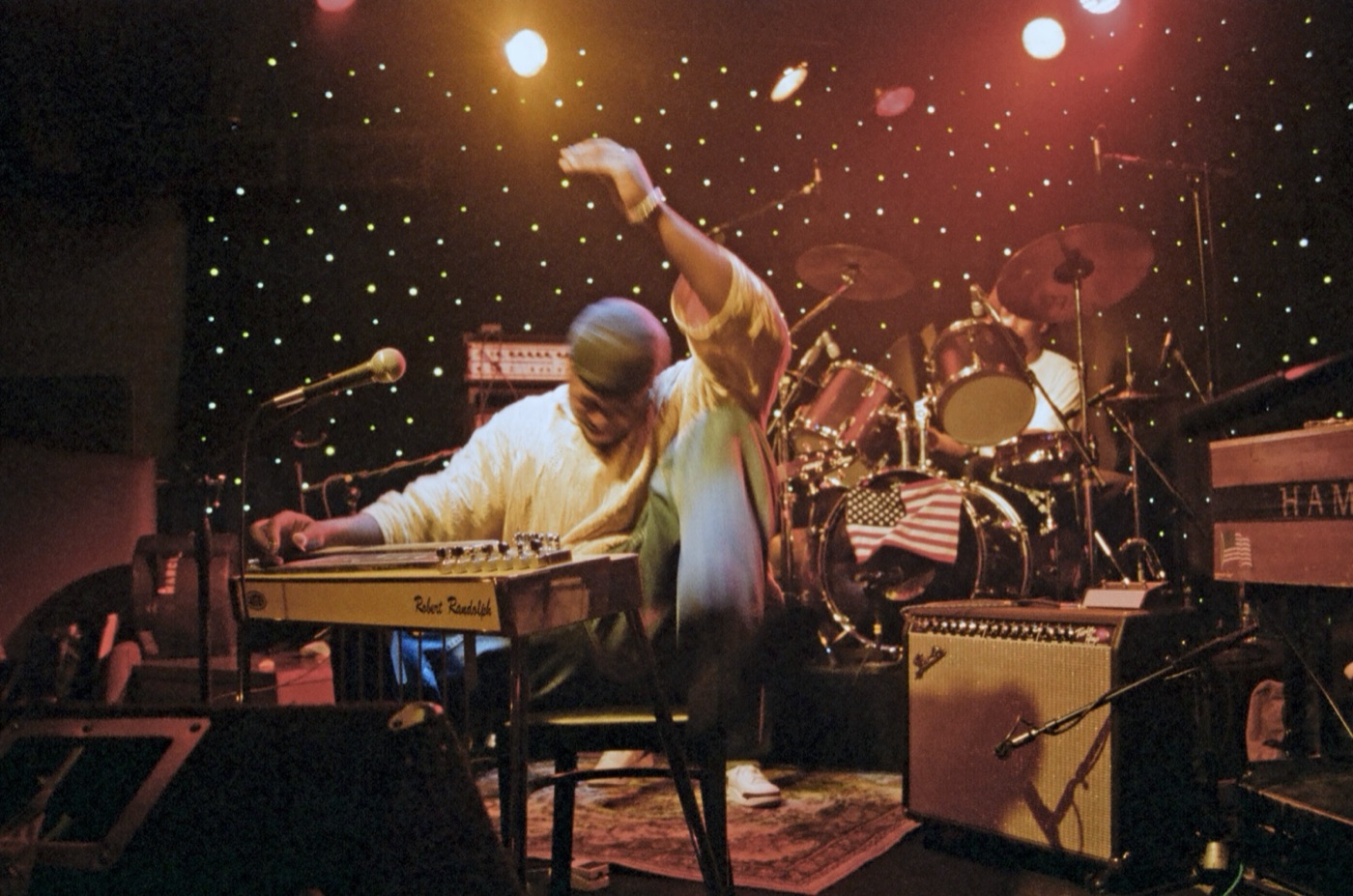 Robert Randolph throws one arm high over his pedal steel as spotlights and a starry curtain glow behind the drum kit.