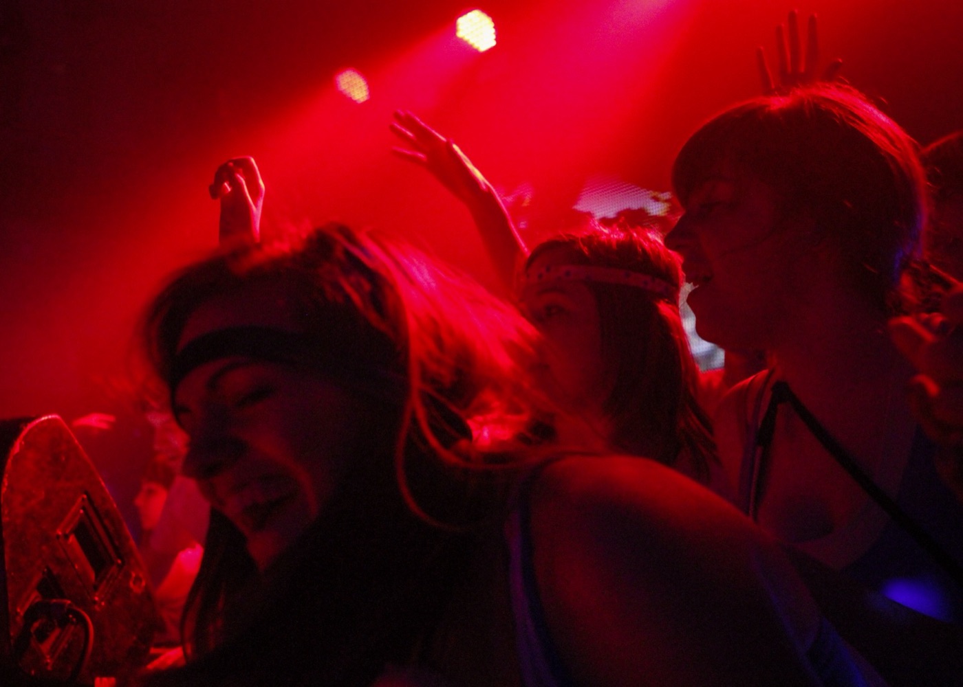 Dancers in headbands move under red stage lights with hands raised behind them.