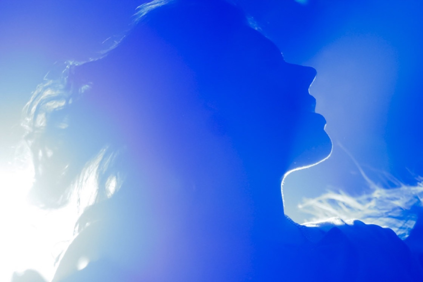 A dancer's face in profile turns up into a wash of blue stage light, her outline traced in white.